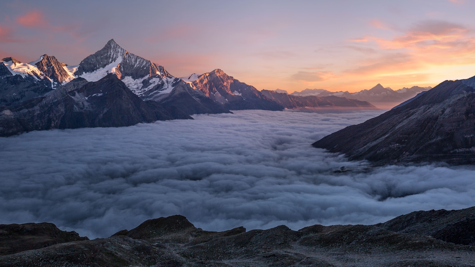 A calm mountain lake at sunrise with mist rising over still water.